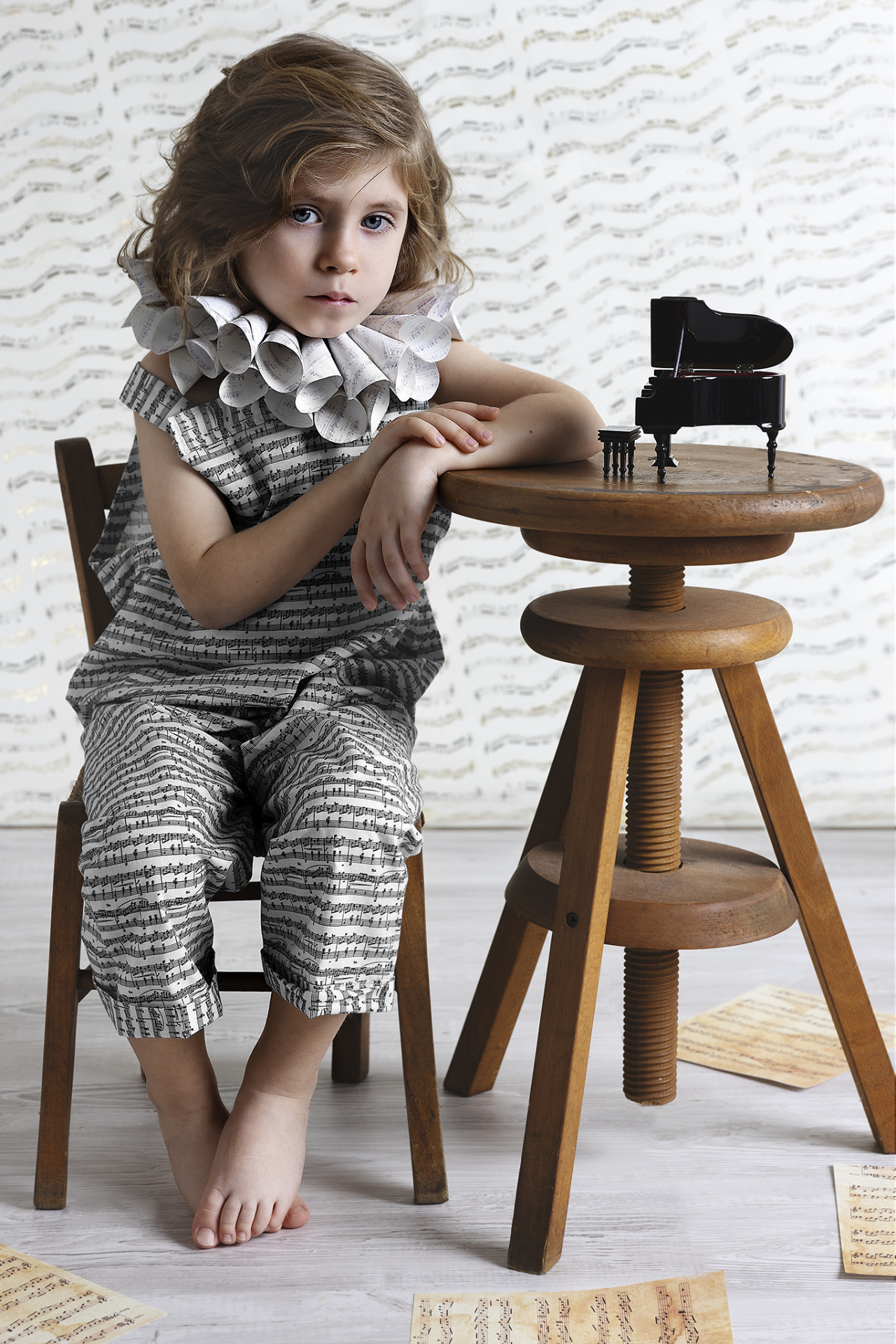 Ritratto artistico di bambino in abito con motivi musicali e spartiti sparsi, su sfondo tematico, realizzato da Claudia Spaziani a Bologna.