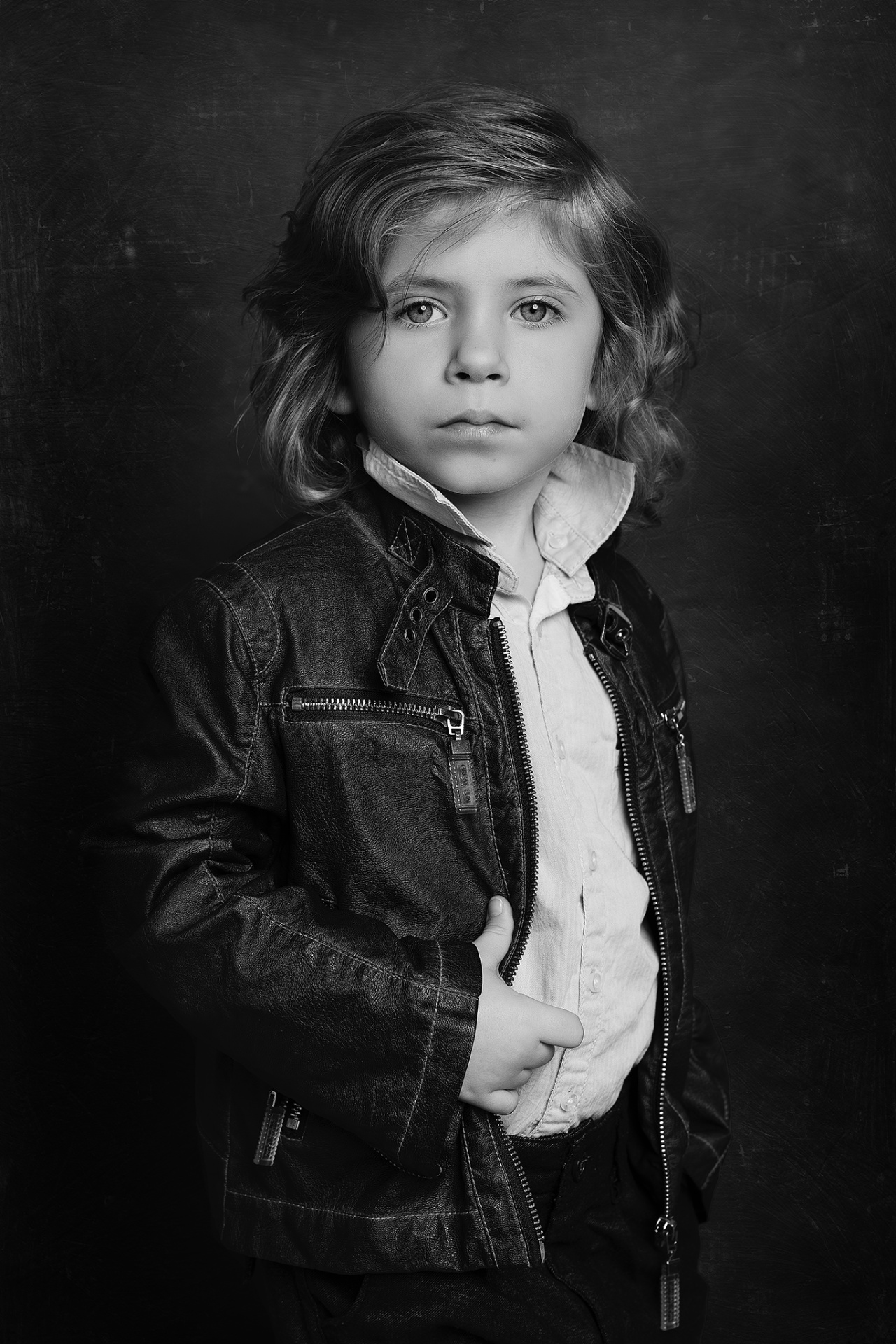 Ritratto monocromatico di bambino con giacca in pelle e camicia, su sfondo scuro, scattato da Claudia Spaziani nel suo studio fotografico a Bologna.