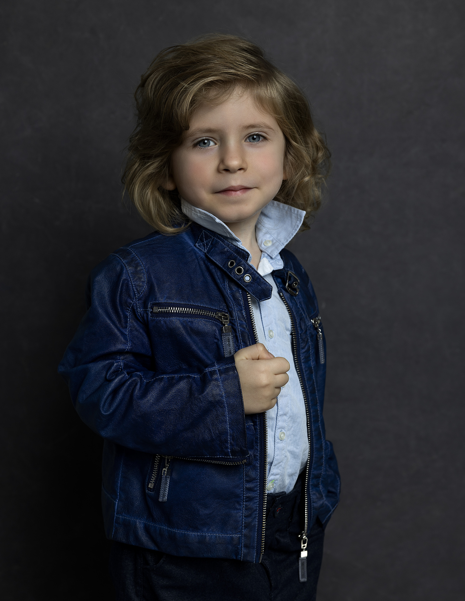 Ritratto moderno di bambino con giacca in pelle blu e camicia azzurra, su sfondo scuro, realizzato da Claudia Spaziani nel suo studio fotografico a Bologna.