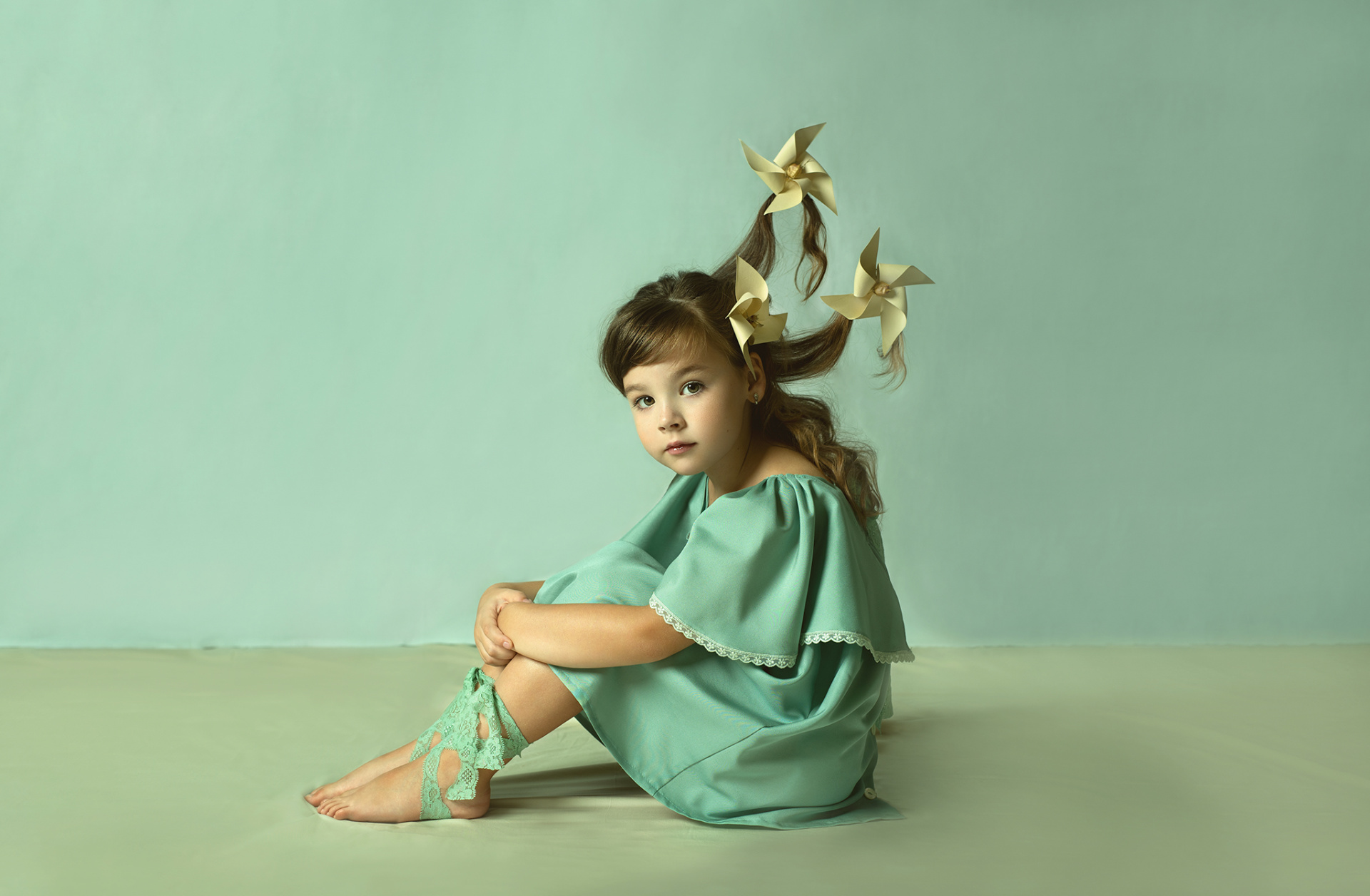 Ritratto artistico di bambina in verde menta con girandole nei capelli, su sfondo monocromatico, scattato da Claudia Spaziani nel suo studio fotografico a Bologna.
