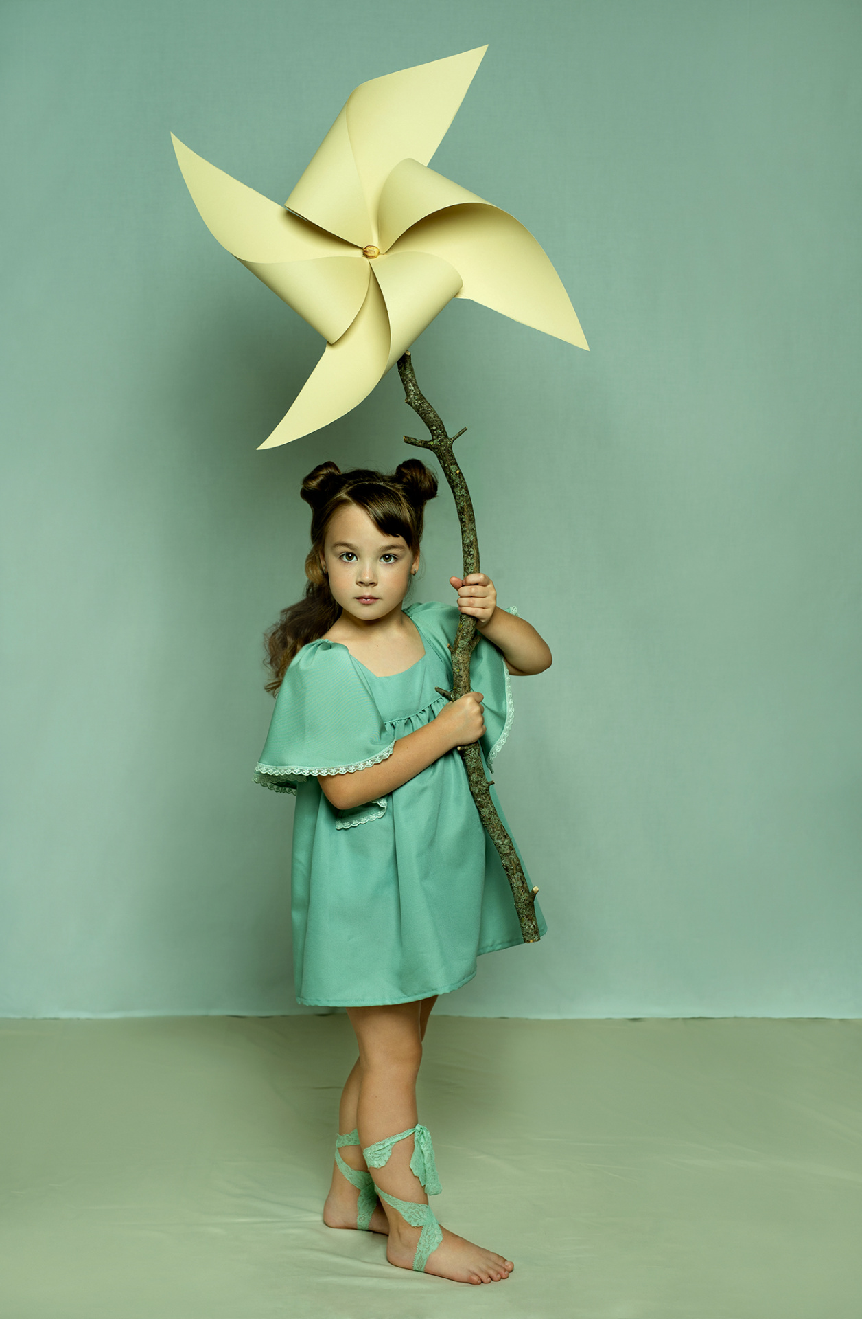 Ritratto fiabesco di bambina in abito verde con girandola gialla su ramo naturale, scattato da Claudia Spaziani nel suo studio fotografico a Bologna.