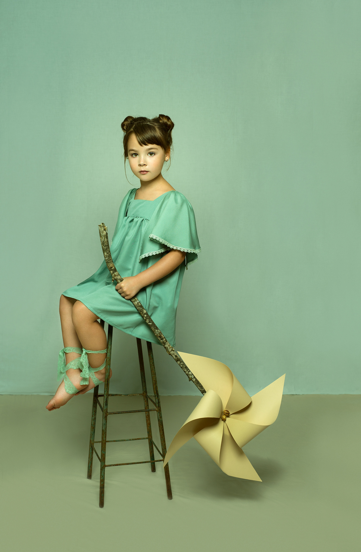 Ritratto creativo di bambina in abito verde menta con girandola gigante, su sfondo monocromatico, scattato da Claudia Spaziani nel suo studio fotografico a Bologna.