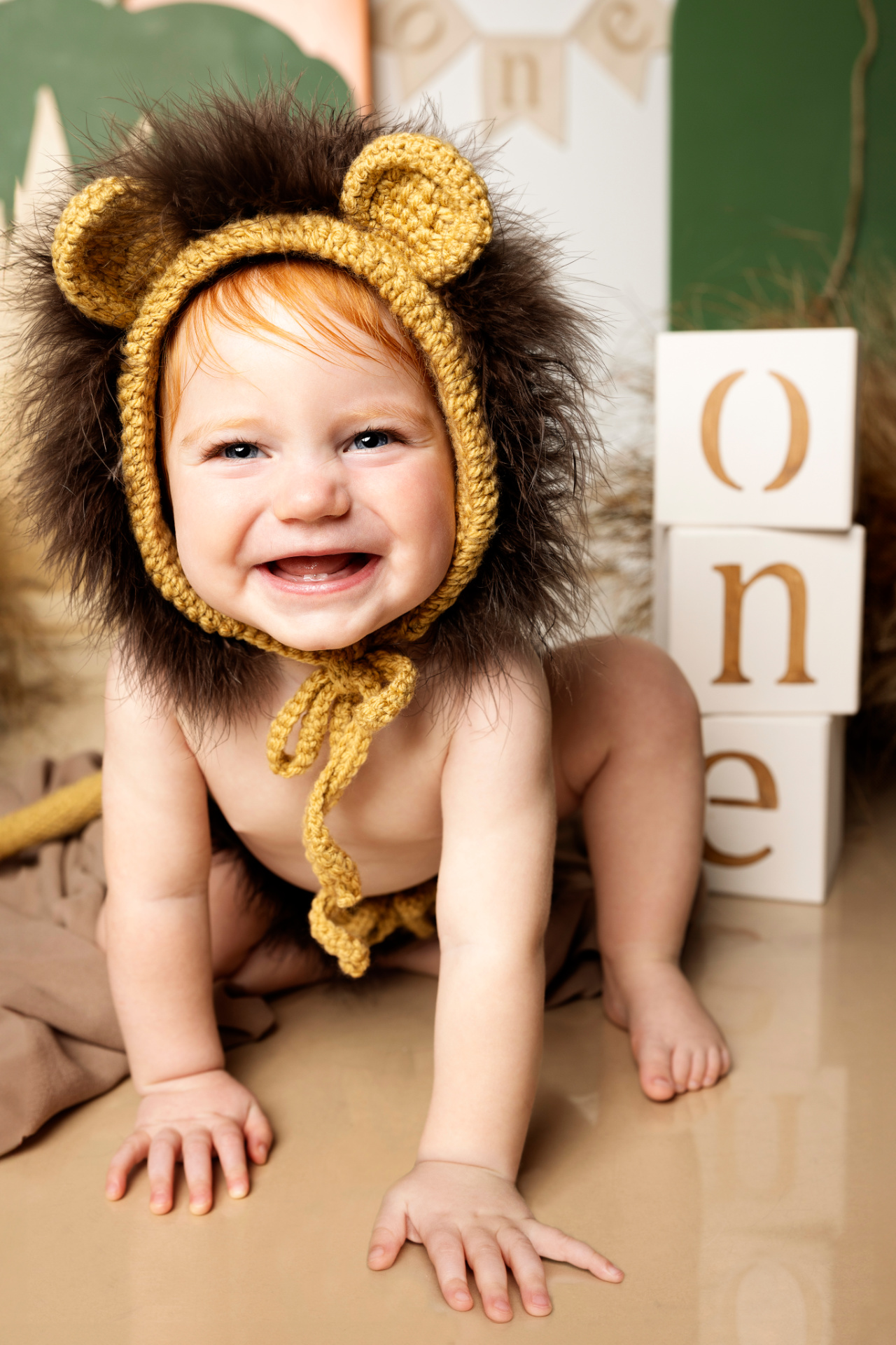 Bambina in costume da leoncino con cappello a criniera, sorridente davanti a blocchi "ONE" e decorazioni verdi. Foto di primo compleanno a tema animale realizzata da Claudia Spaziani nel suo studio fotografico a Bologna.