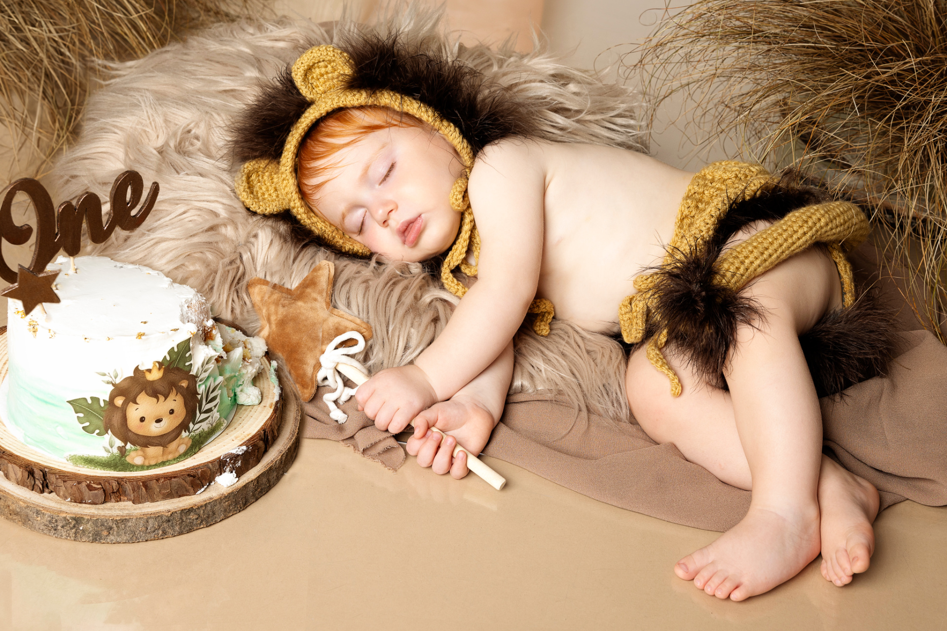 Bambina vestita da leoncino dorme accanto a torta decorata con topper "One" e illustrazione di leone. Atmosfera calda e naturale. Ritratto di primo compleanno scattato da Claudia Spaziani nel suo studio fotografico a Bologna.