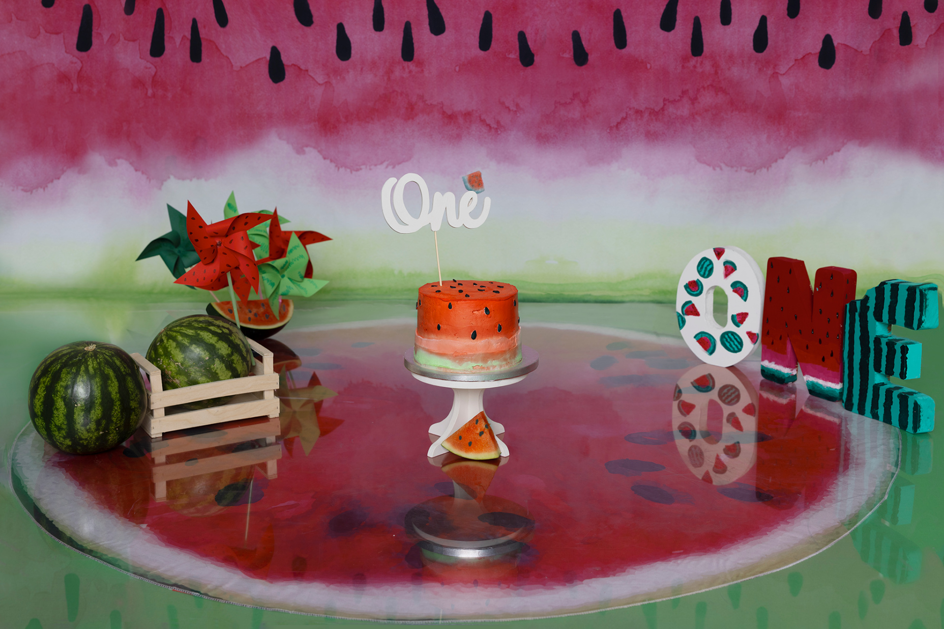 Torta decorata come anguria con topper "One", circondata da angurie vere, girandole e lettere "ONE" a tema. Foto di primo compleanno creativa scattata da Claudia Spaziani, fotografa ritrattista a Bologna.