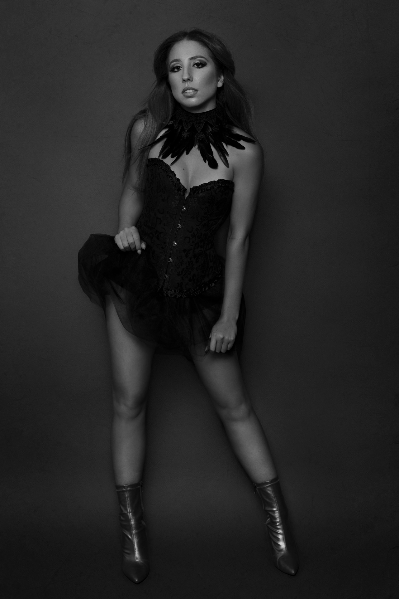 Ritratto glamour in bianco e nero di una donna in posa teatrale con corsetto ricamato nero, gonna in tulle e stivaletti metallici, impreziosita da un accessorio piumato al collo. Fotografia fine art realizzata da Claudia Spaziani nel suo studio a Bologna.