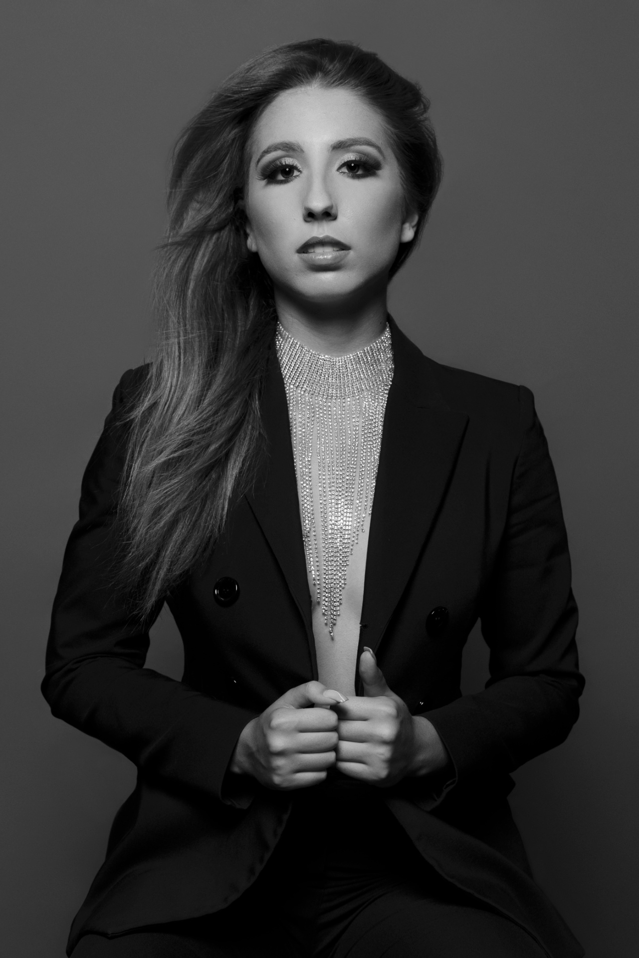 Ritratto creativo in bianco e nero di una donna seduta con blazer doppiopetto senza camicia, indossando una collana scultorea a fili lucenti. Sguardo deciso e styling elegante. Fotografia fine art glamour di Claudia Spaziani, Bologna.