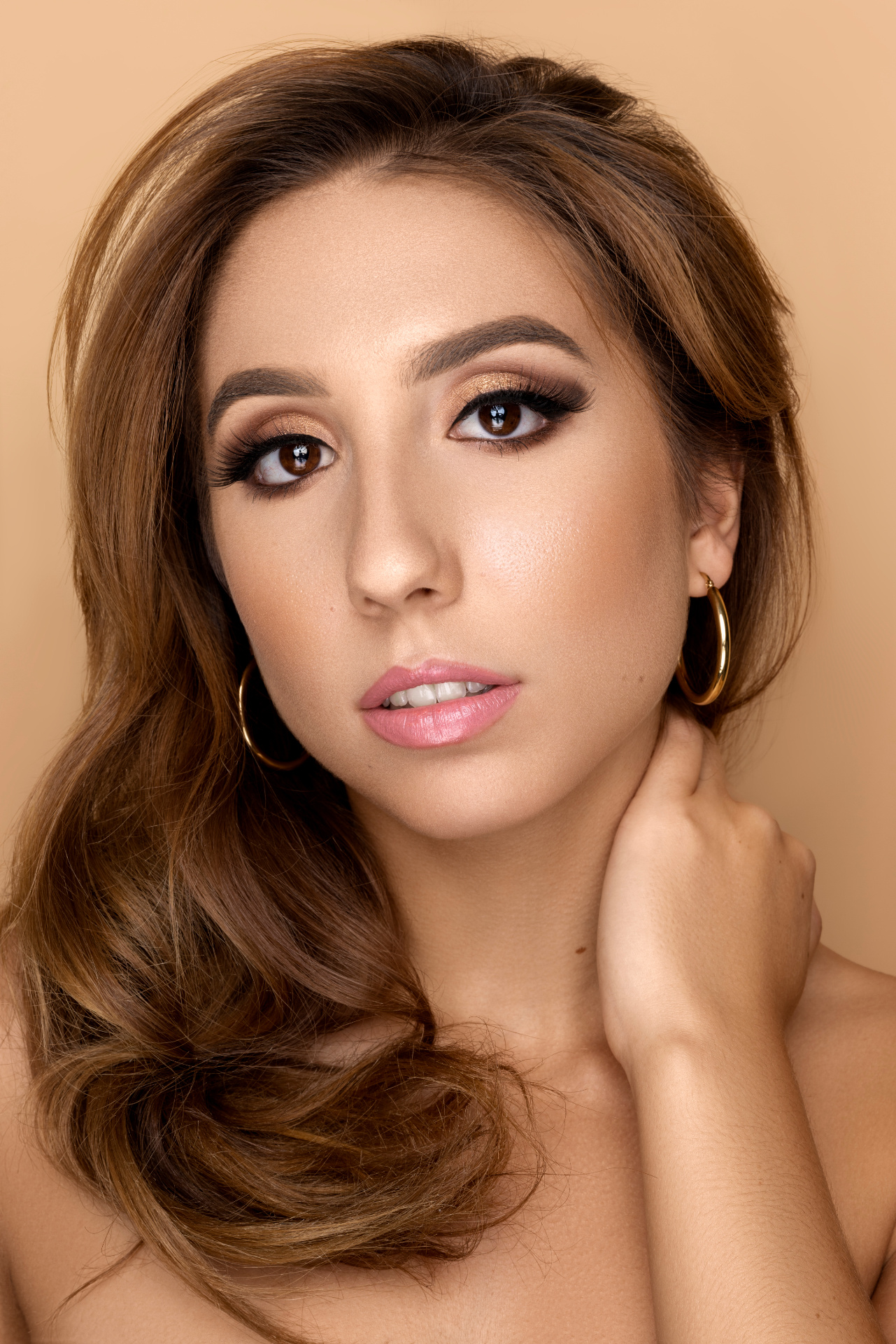 Ritratto beauty fine art di una donna con capelli ondulati castani, pelle luminosa e trucco raffinato. Sfondo beige e sguardo diretto in camera. Fotografia glamour realizzata da Claudia Spaziani nel suo studio a Bologna.