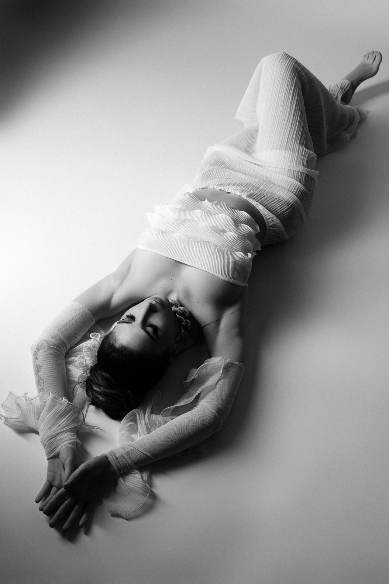 Ritratto fine art scattato da Claudia Spaziani vicino a Bologna; outfit plissé con top a rouches e pantaloni coordinati, posa distesa vista dall’alto e atmosfera sofisticata.