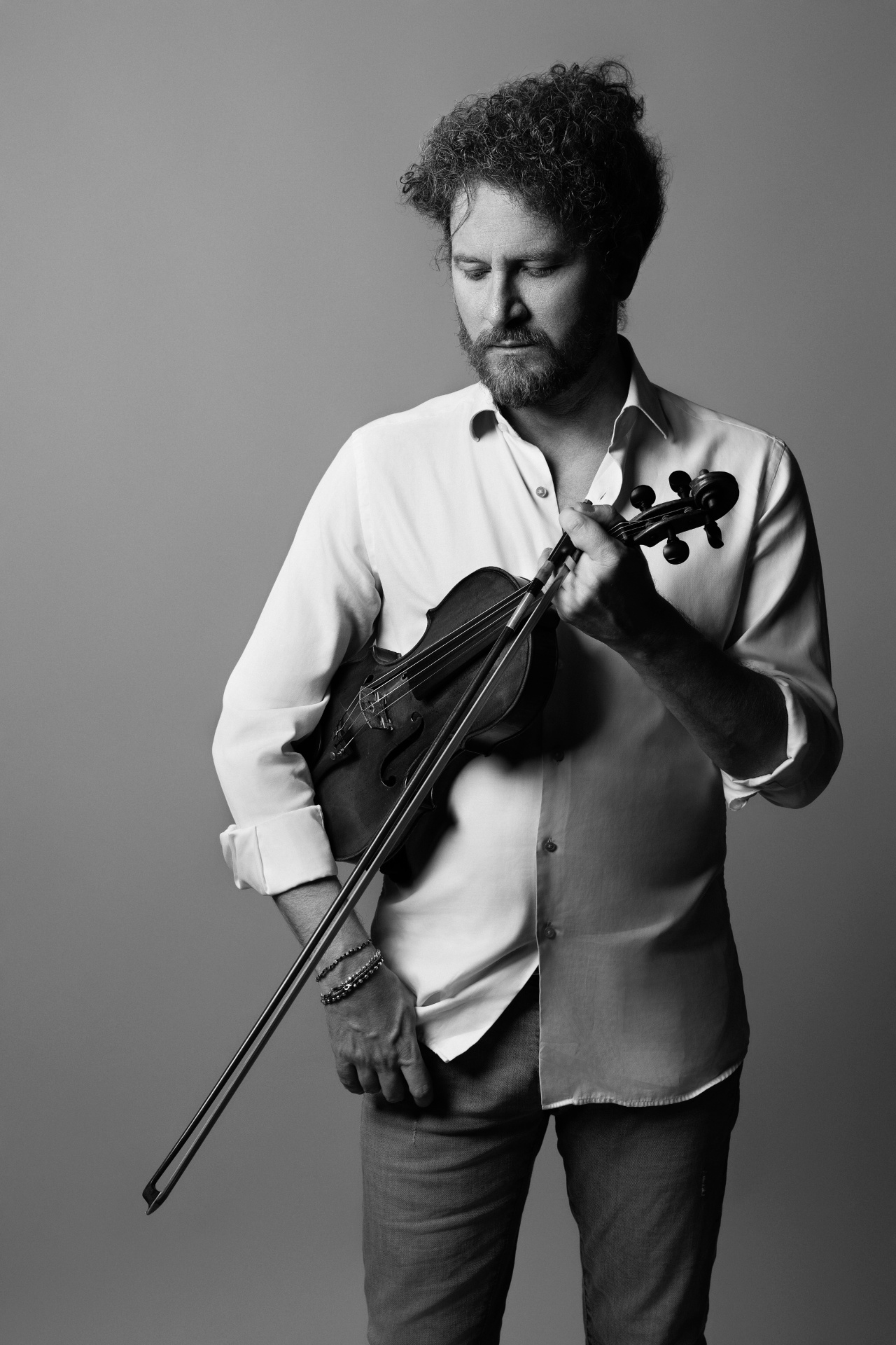 Marco, violinista, in bianco e nero con camicia bianca e violino tenuto al fianco con sguardo verso il basso, ritratto fine art per book di Claudia Spaziani a Bologna.