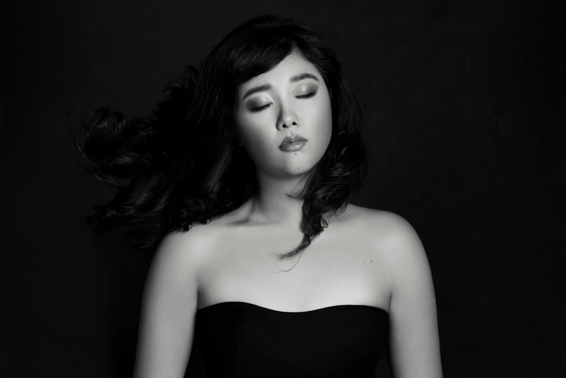 Yuwei, cantante lirica, in bianco e nero con capelli in movimento e trucco intenso, ritratto fine art per book professionale di Claudia Spaziani a Castel Guelfo, Bologna.