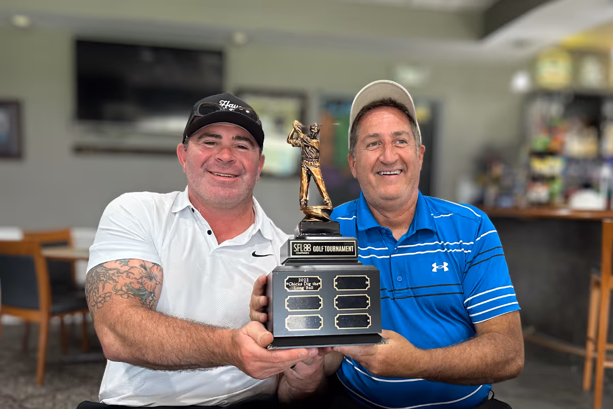 Two golfers smiling with SFL 88 Golf Tournament trophy in office