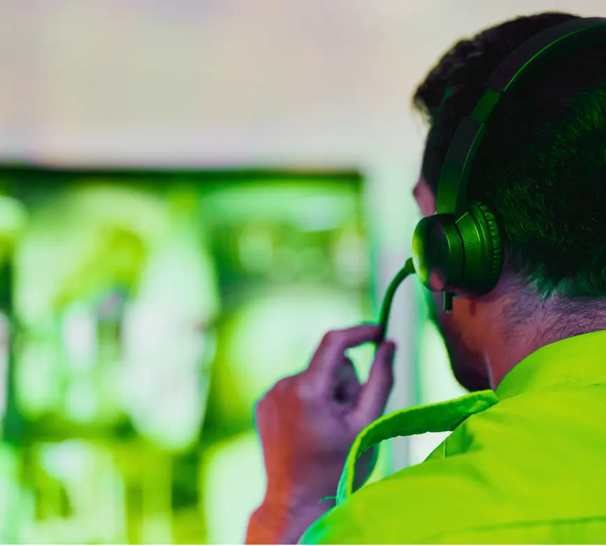 Operator wearing a headset, speaking into the mic while watching screens in green-tinted light.