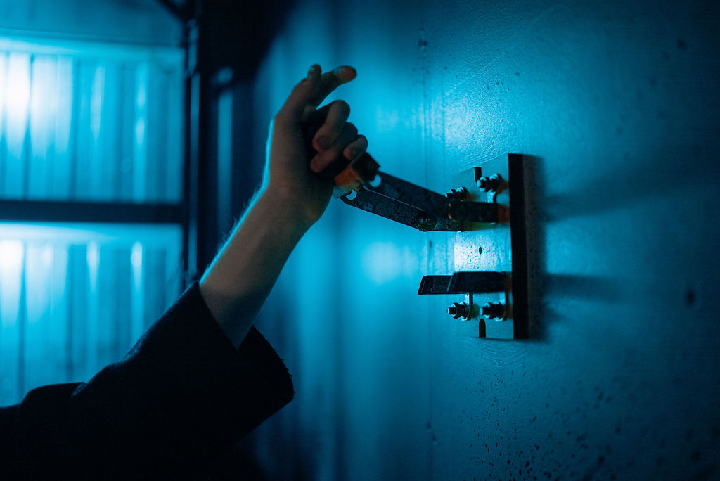 A hand pulling an old-fashioned knife switch attached to a wall against an industrial background with cool blue lighting.