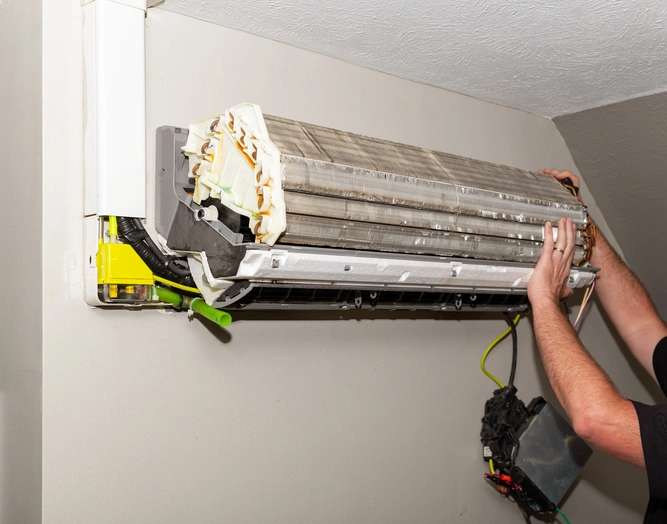A person repairs a wall-mounted air conditioning unit, with the front panel removed. 