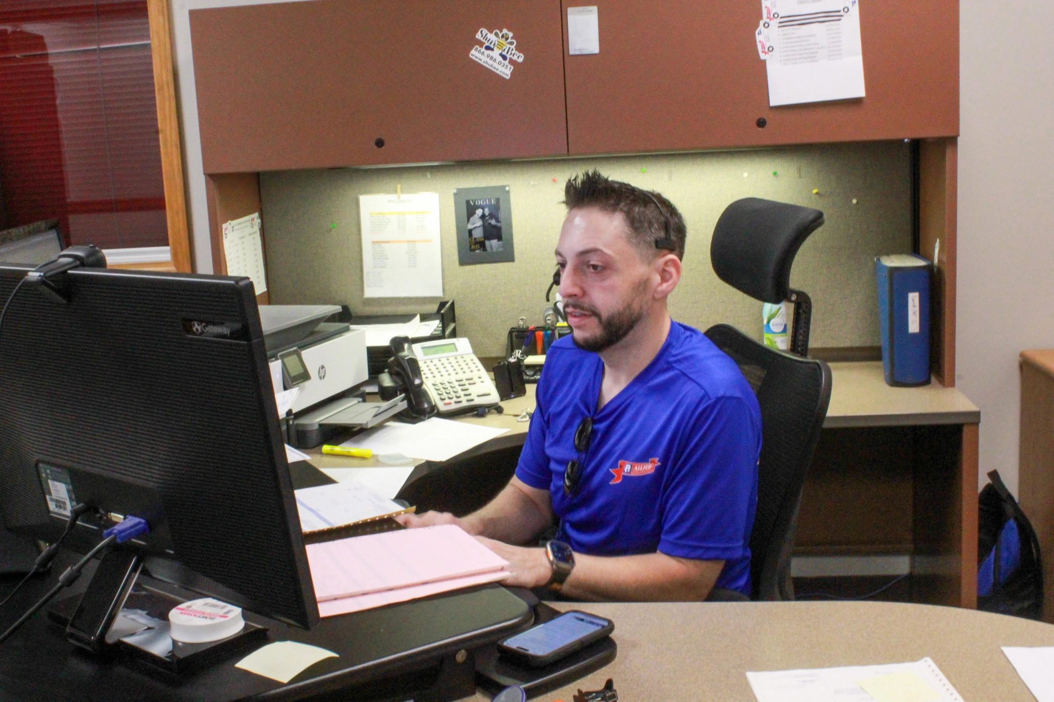 Man in a blue shirt sits at a desk, focused on a computer screen. 