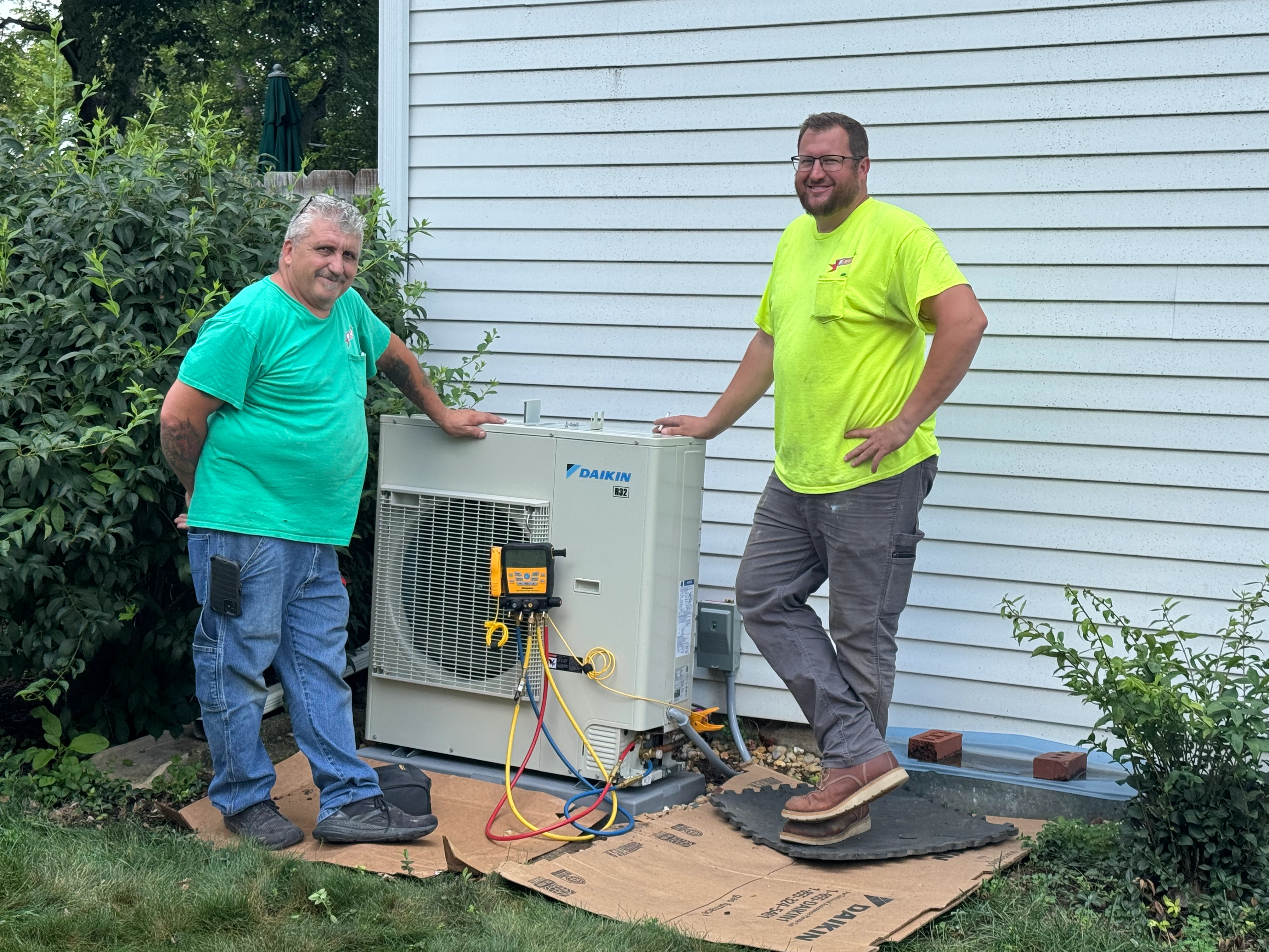 Two men smiling beside a newly installed Daikin HVAC system against a white house.