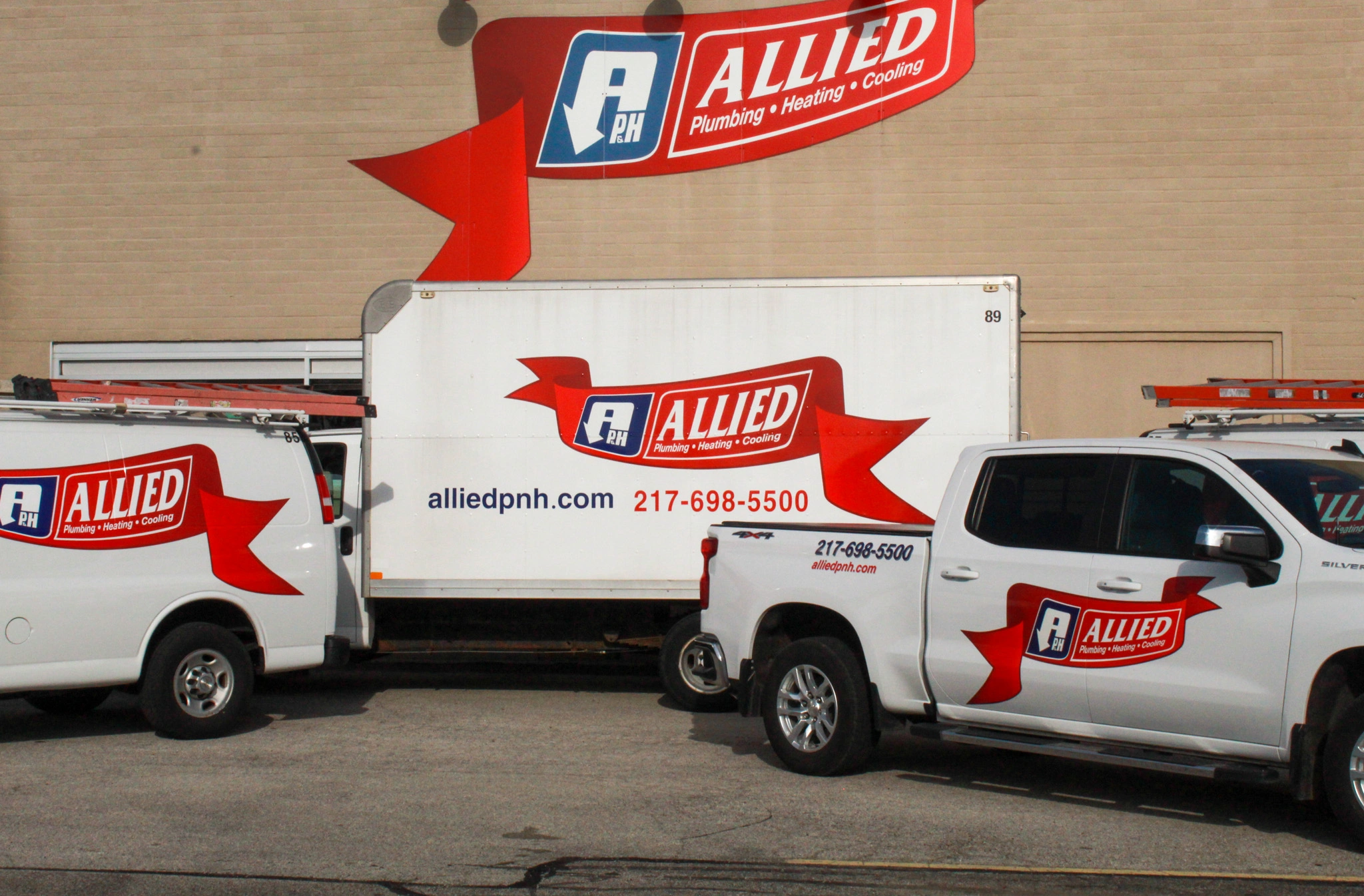 Three white utility vehicles, featuring "Allied Plumbing, Heating & Cooling" logos with red banners,