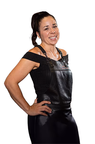 Femme souriante portant un tablier noir avec les mains sur les hanches.