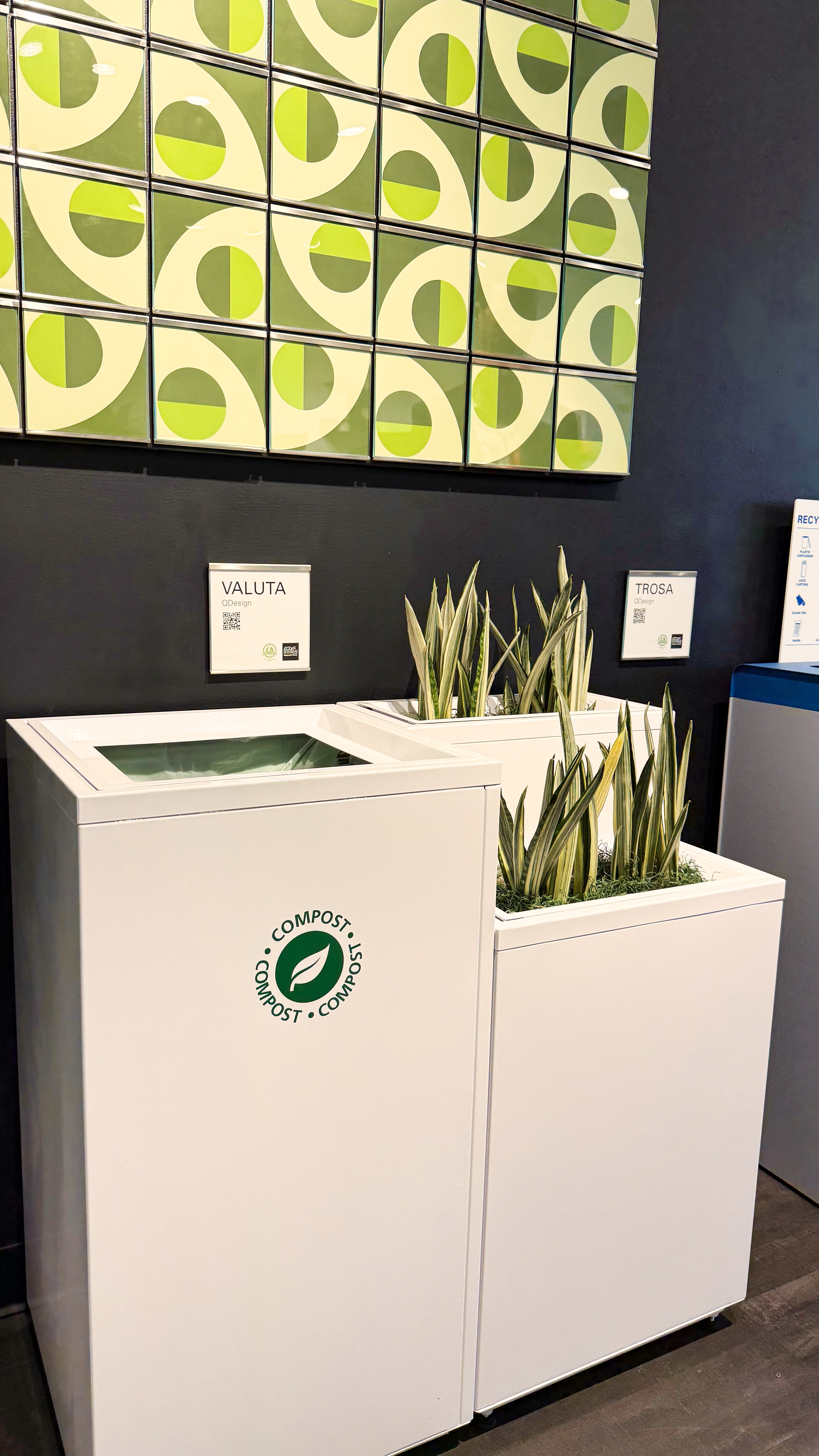 White metal waste basket with two plants in a matching planter by it's side.