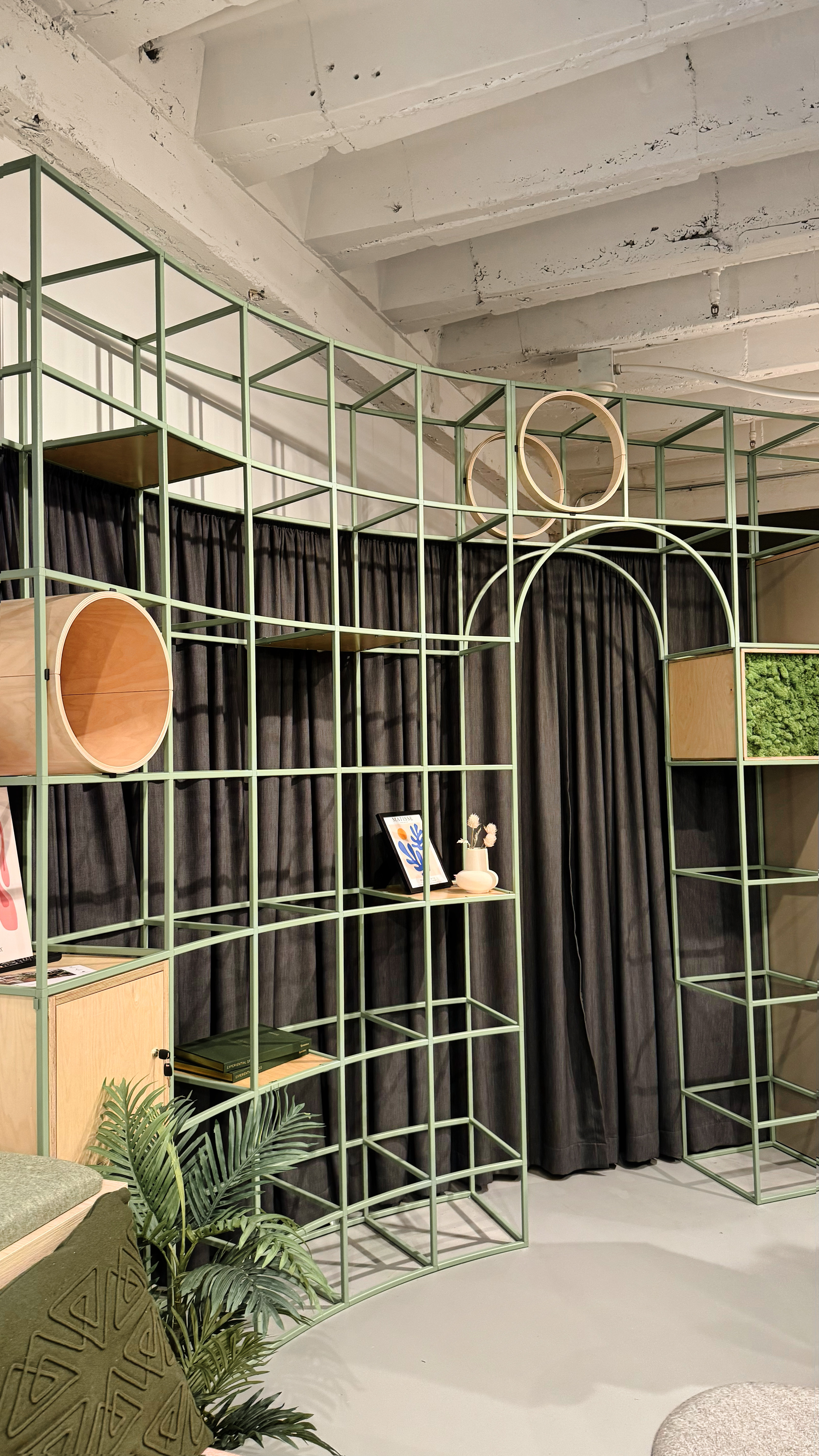 A metal grid like frame with wood cubbies placed into the frame next to a curved entryway cut into the grid.