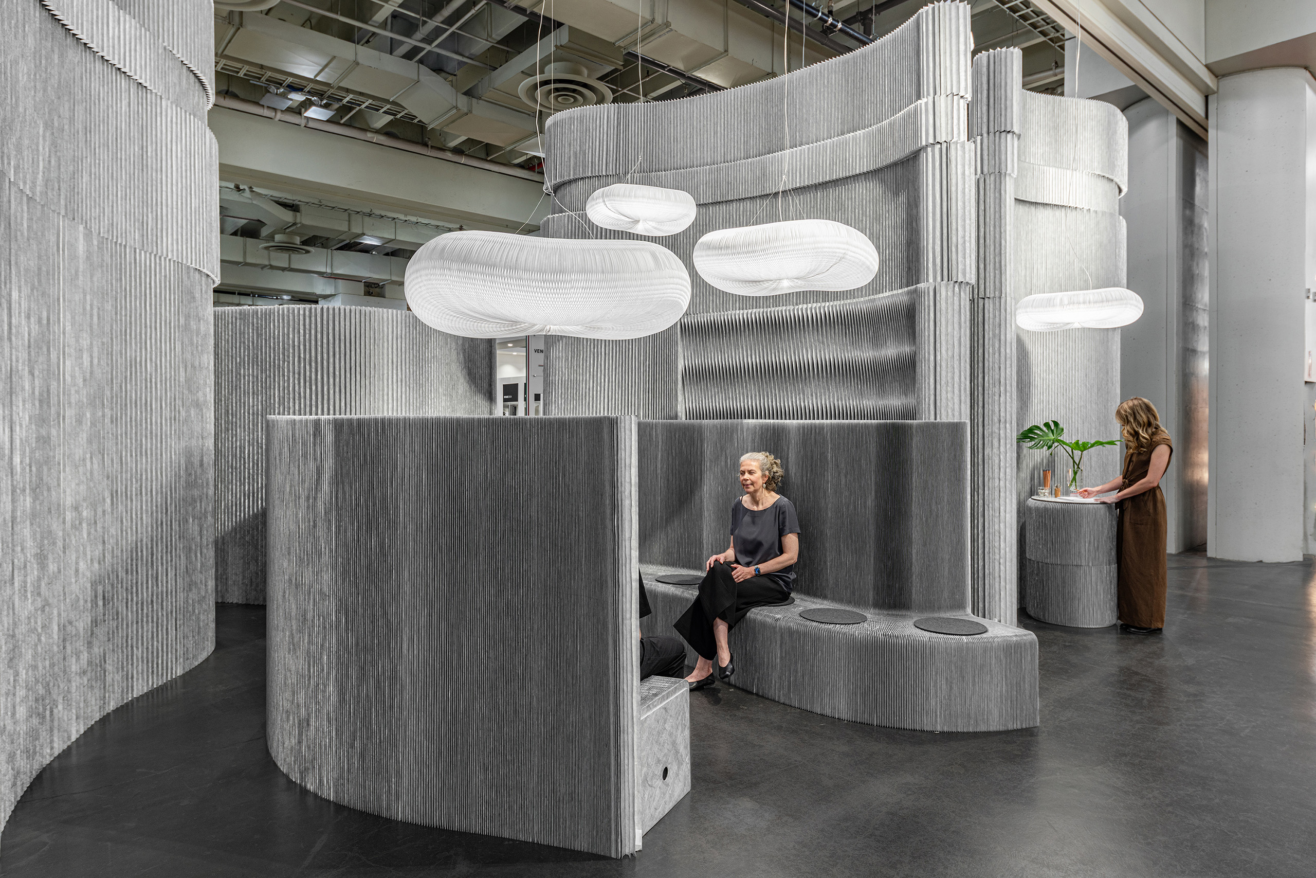 Gray accordion paper wall with people sitting on paper accordion seats.