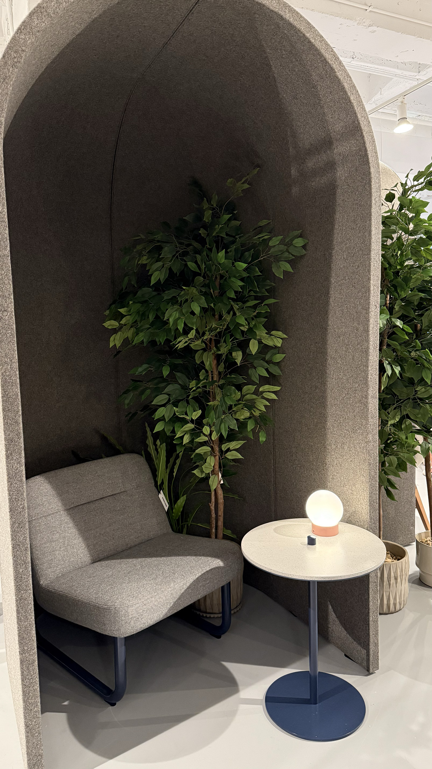 Two felt cylindrical walls joined together to make a half dome. Inside is a chair and a potted tree.