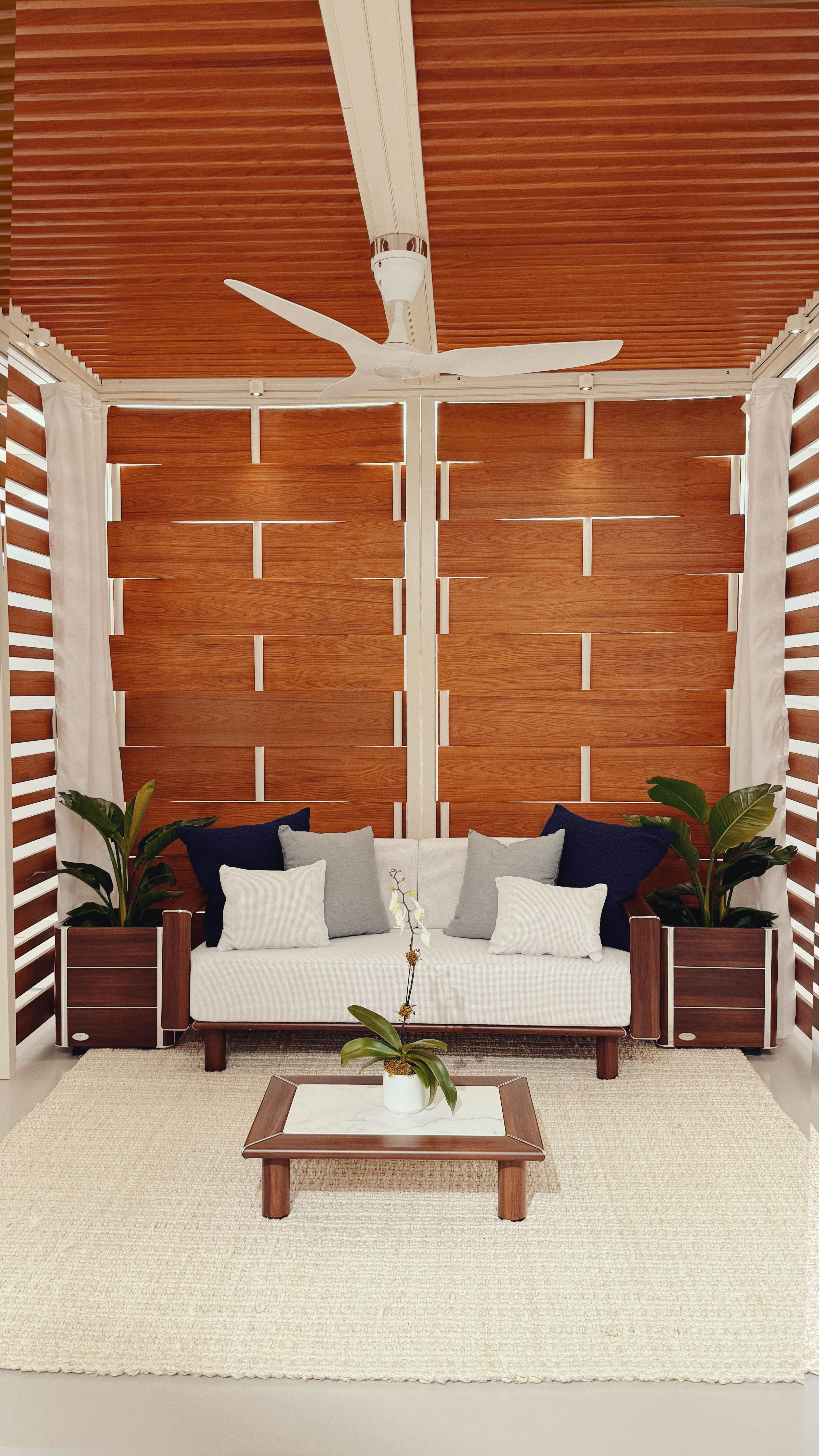 Wood slatted walls and ceiling with a white metal frame, a white ceiling fan, and a white couch.