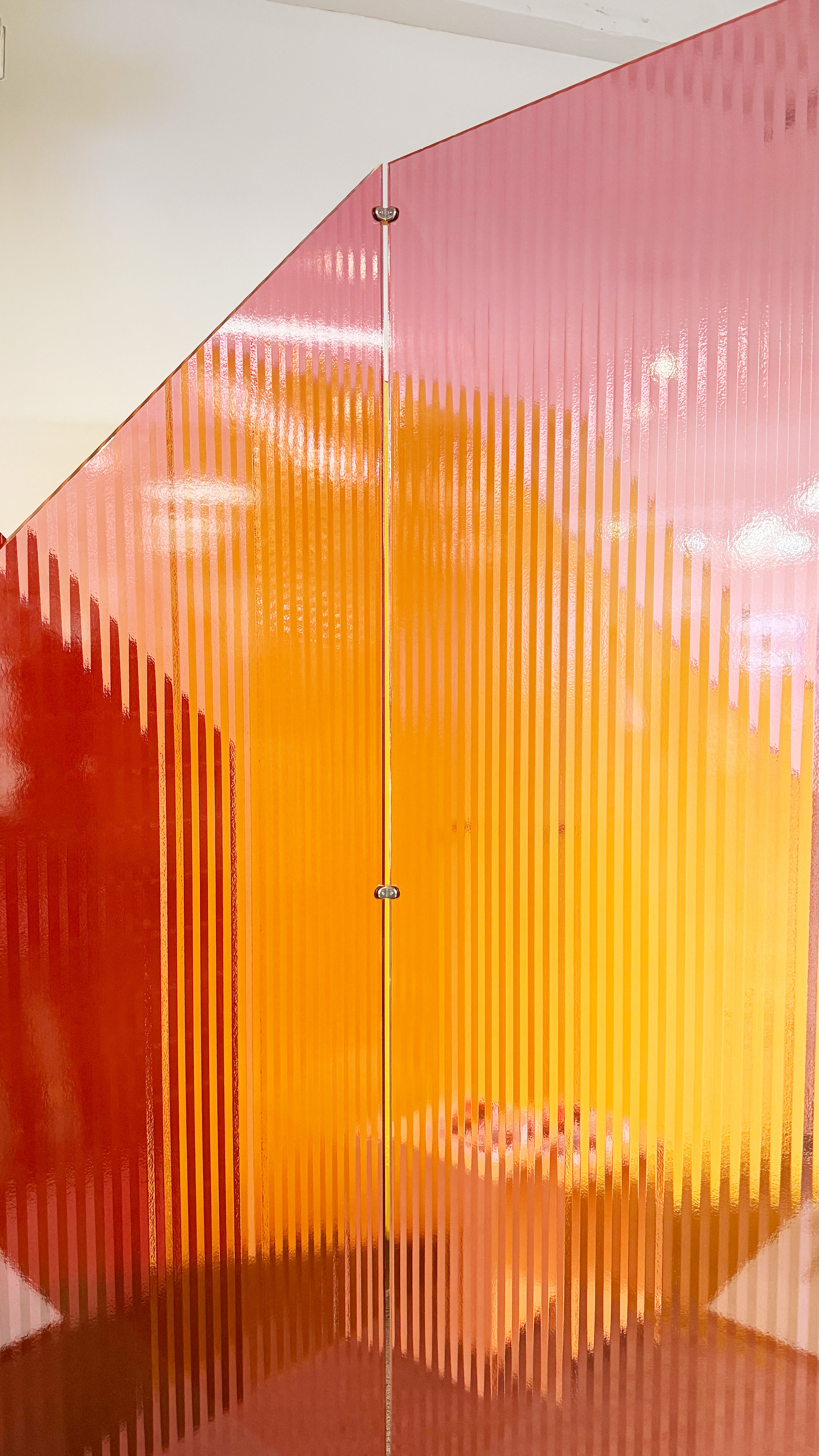 Three plastic opaque walls layered against each other. They are pink, red, and yellow. The 3 layered panels stacked against each other create an array of other colors.
