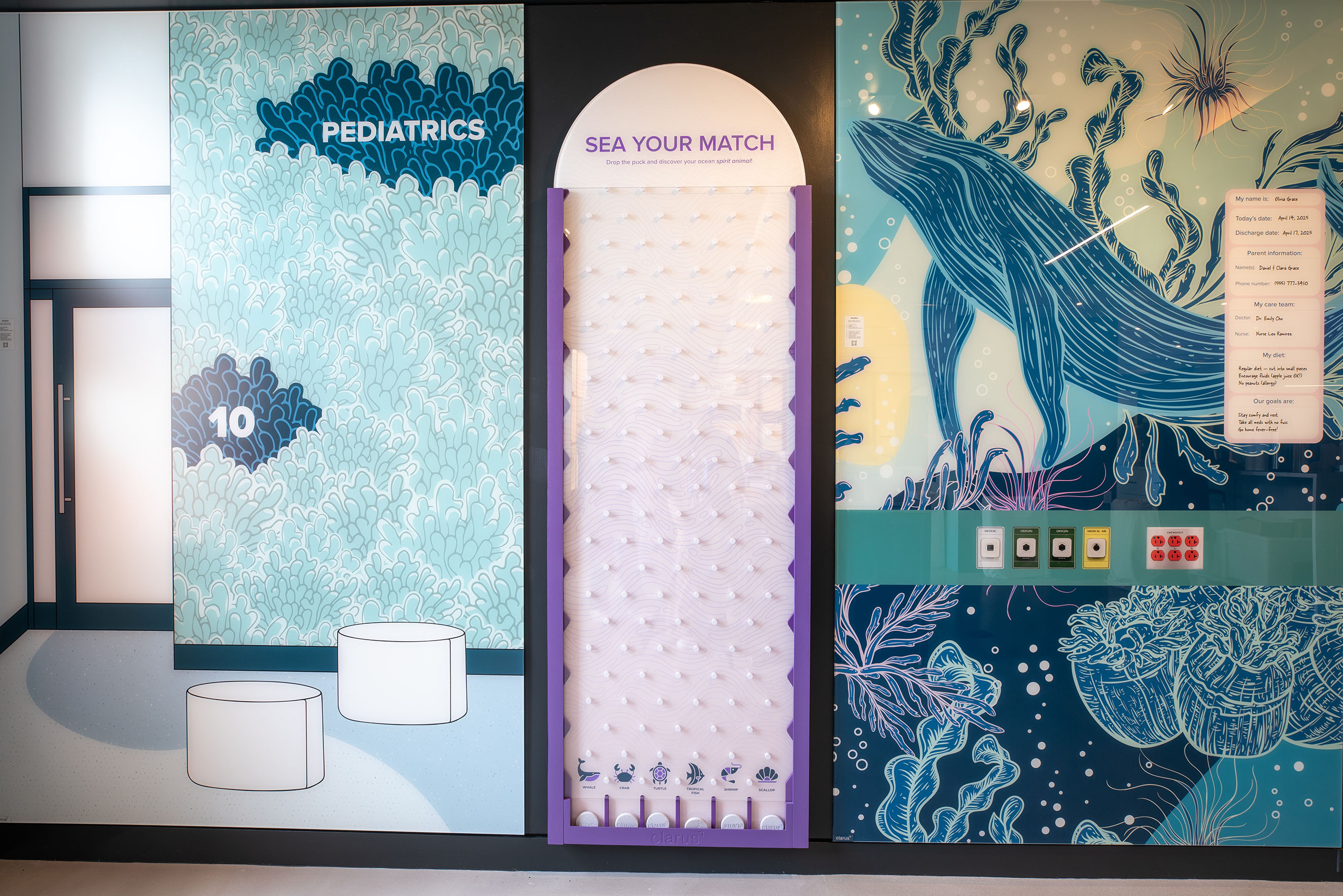 A game of plinko in between two decorative glass boards. One board has a large whale in an ocean landscape with some medical plug-ins and medical charts on top of it. The other board says Pediatrics in an array of coral.