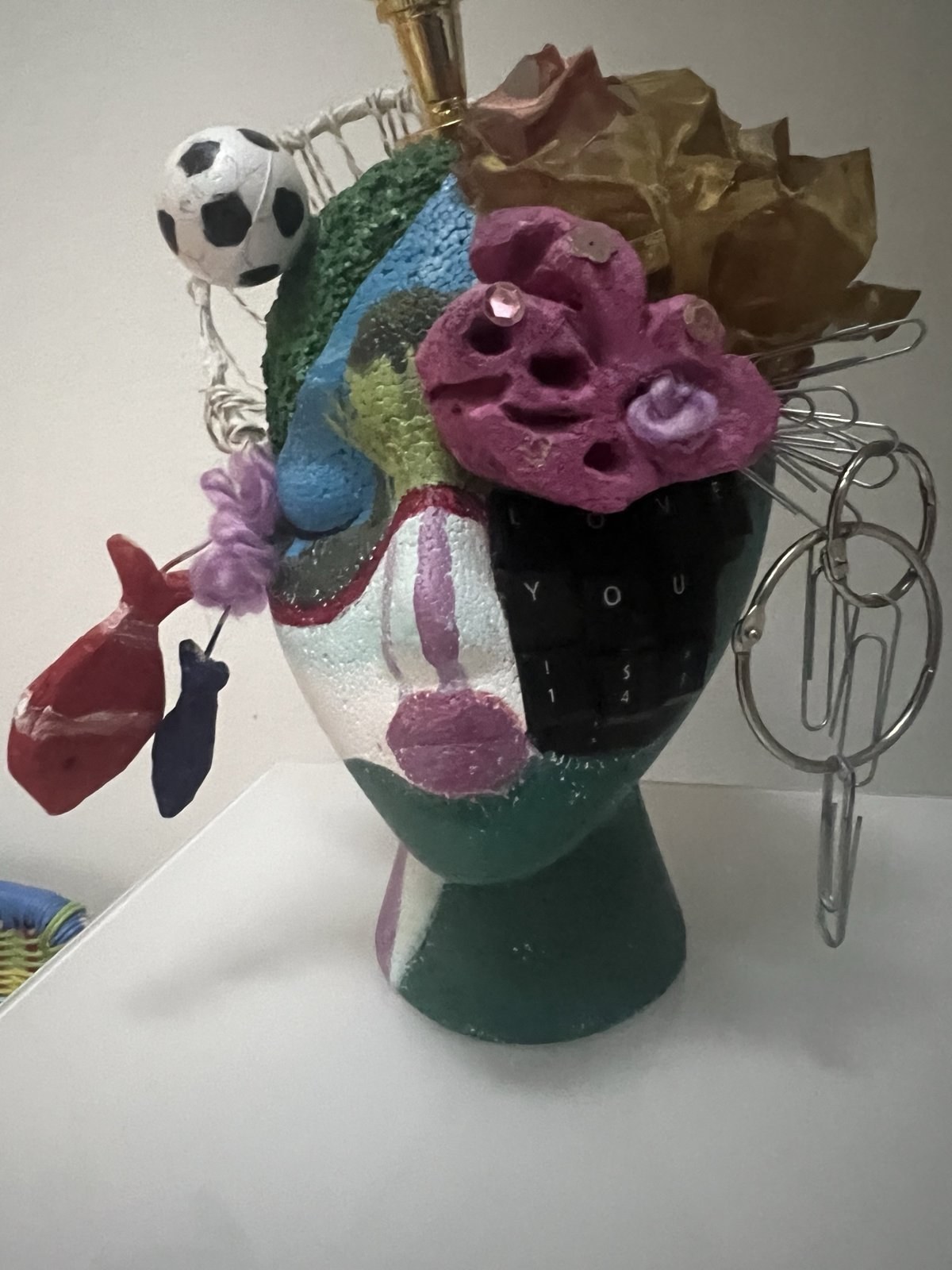 Painted foam head covered with a soccer ball, paper flowers, clay fish, paper clips, key rings and the words love you