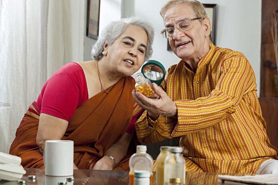 An elderly couple using a magnifying glass to read the description on a bottle of multivitamins for brain health.