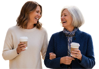 Two women smiling and holding takeaway coffee cups while walking together.