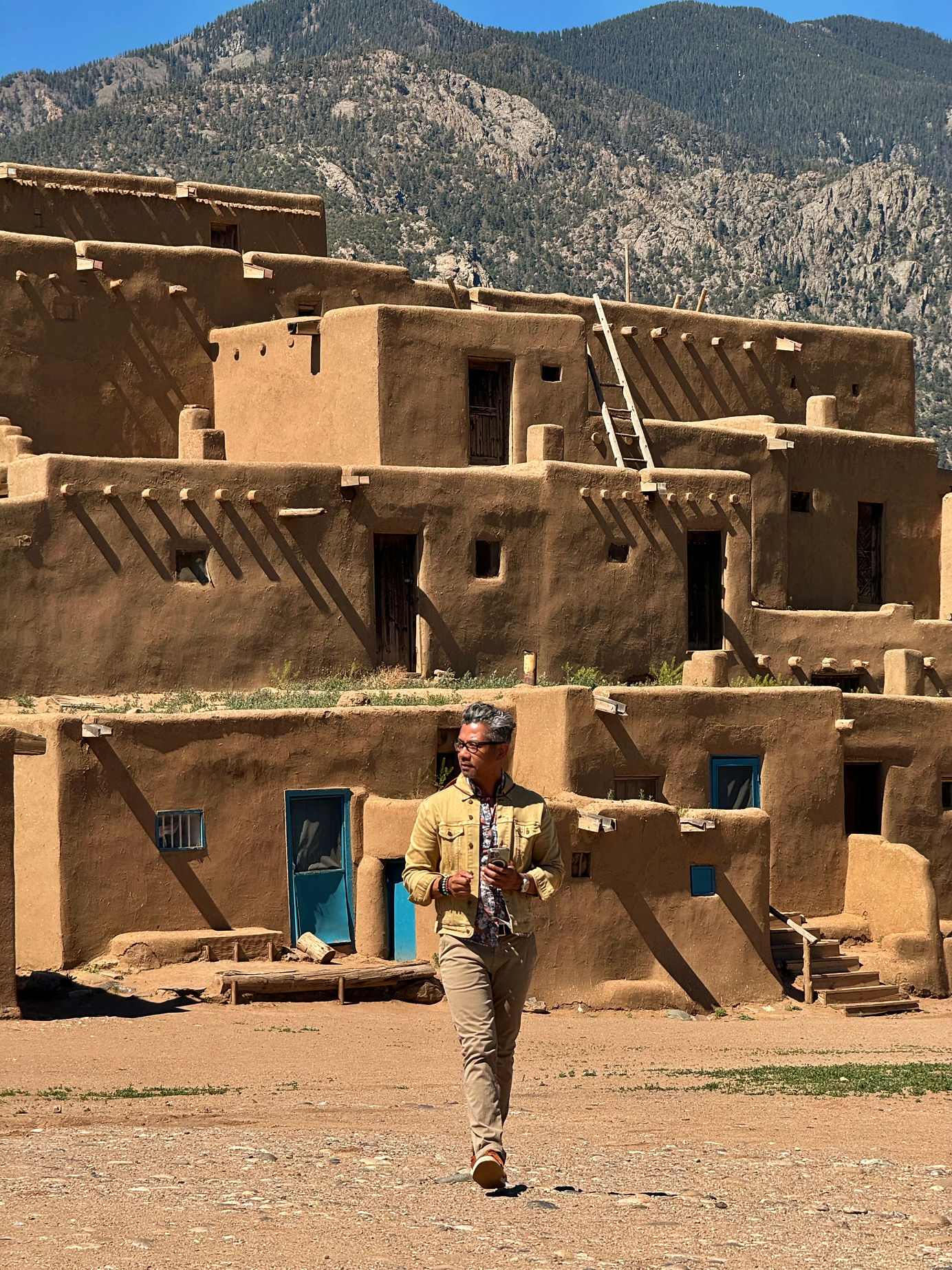 Visitor standing before the historic adobe structures of Taos Pueblo under a clear New Mexico sky