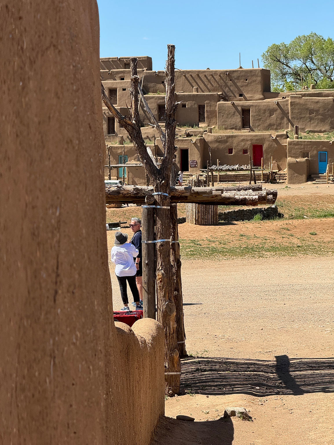 View of friends and adobe buildings at Taos Pueblo framed by sunlit architecture and desert landscape