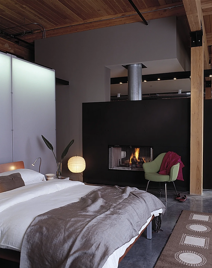 Primary bedroom in a loft featuring a two-sided fireplace and soft layered textures