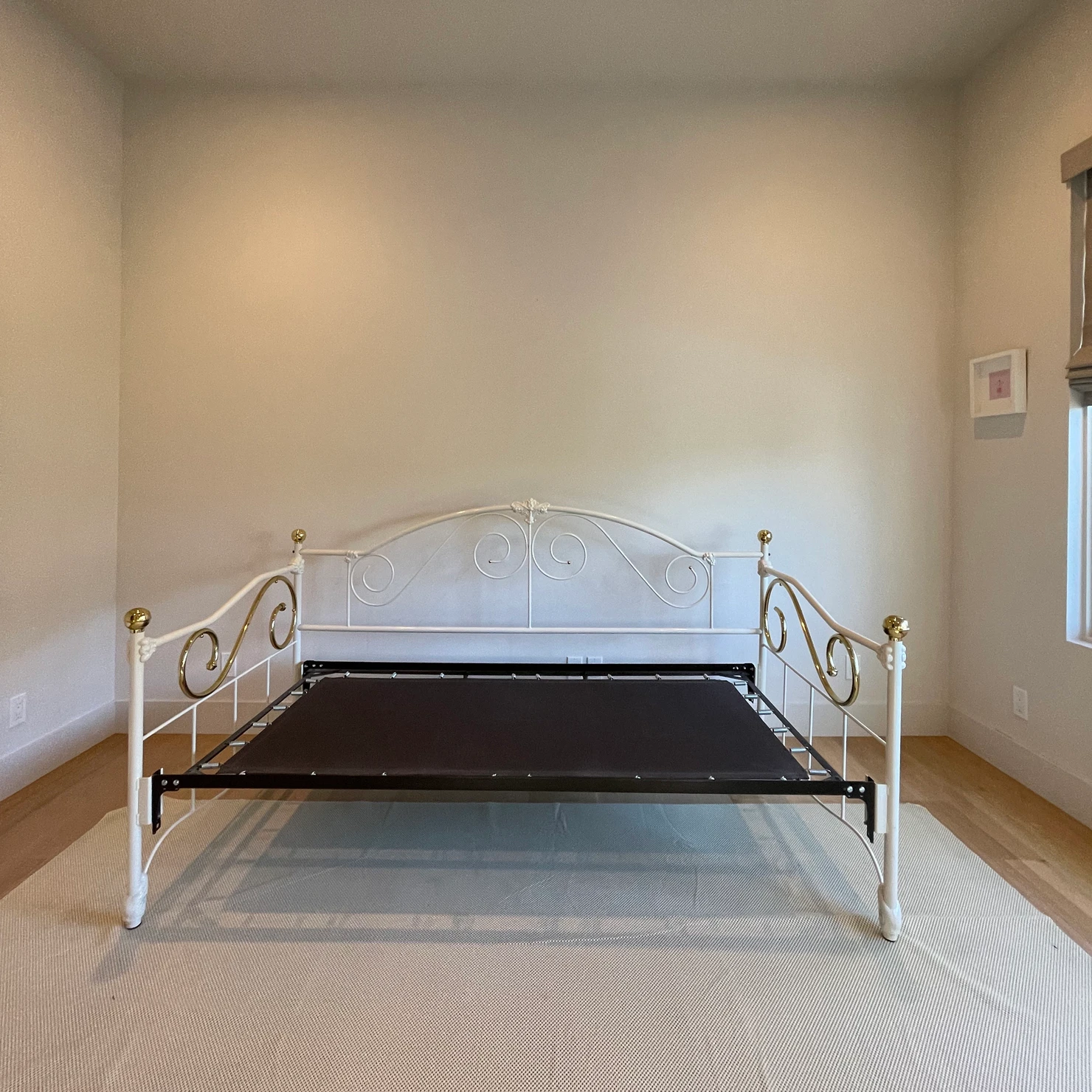 Minimal children’s bedroom with white metal daybed frame centered against a blank wall, showing an empty pre-design space