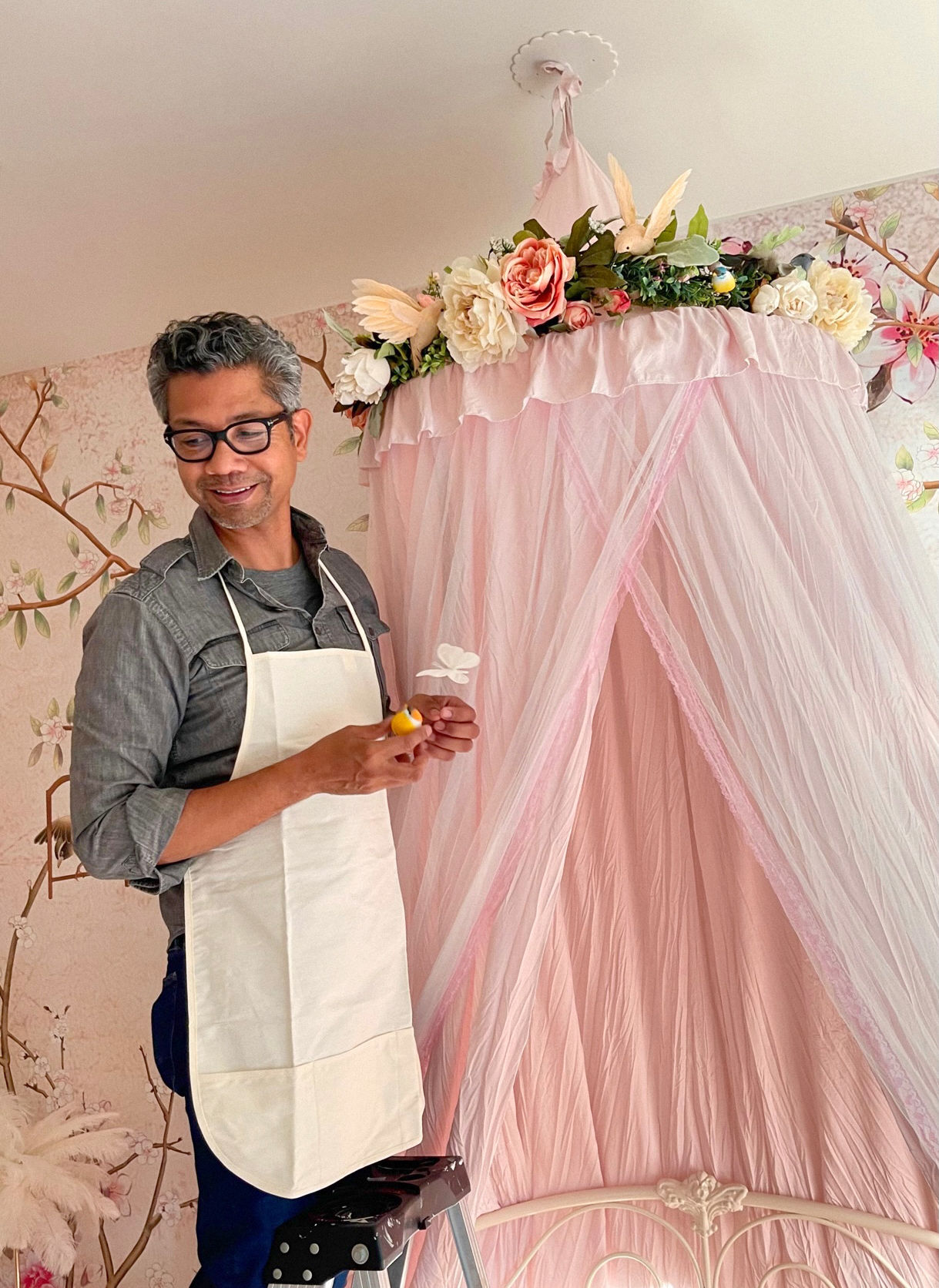 Designer styling a pink canopy with floral garland and bird accents in a whimsical children’s bedroom