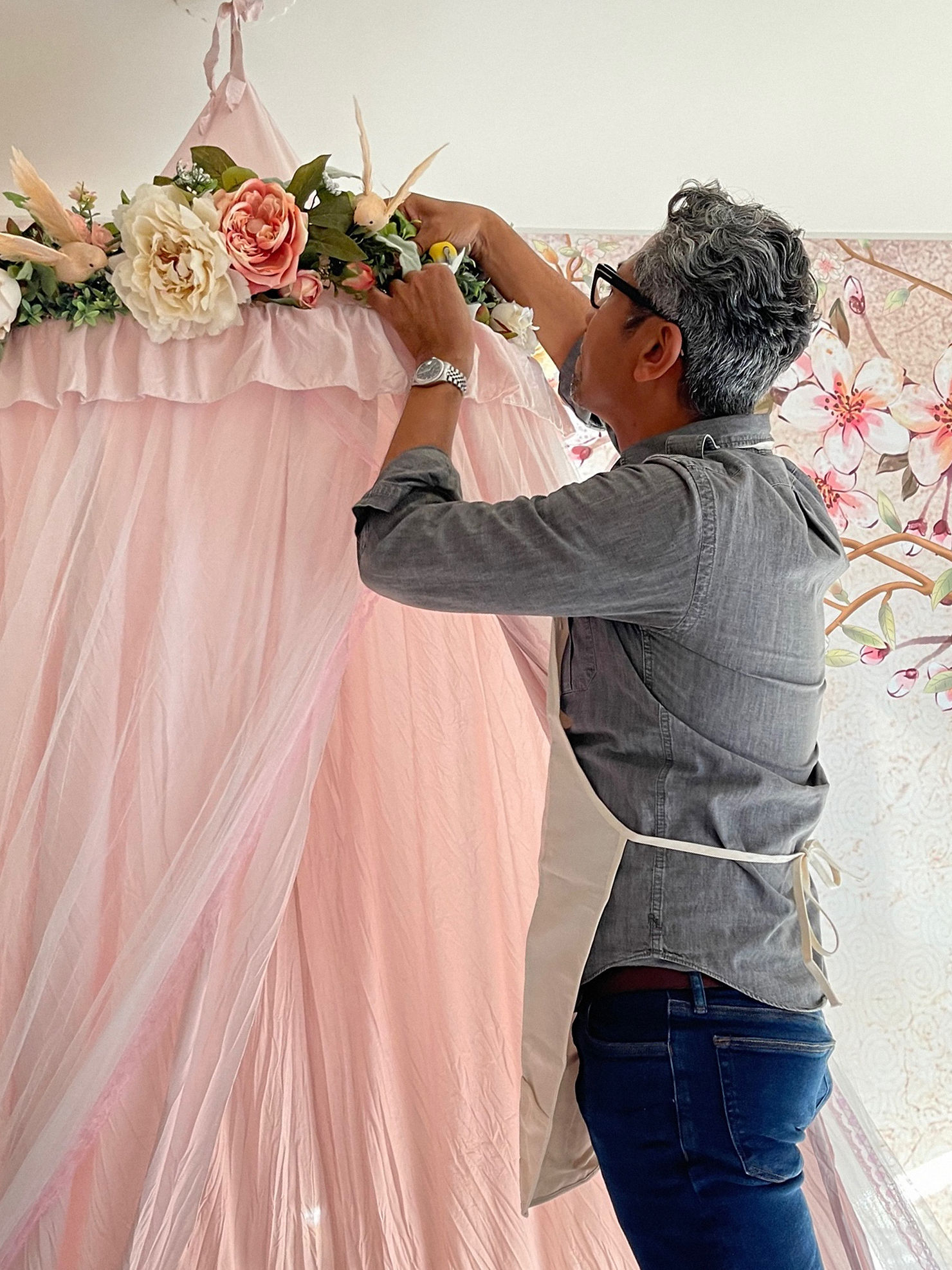 Designer attaching floral and bird accents to a pink canopy, adding decorative details in a child’s bedroom