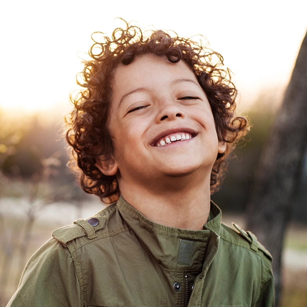 A young boy smiling with a sunset background.