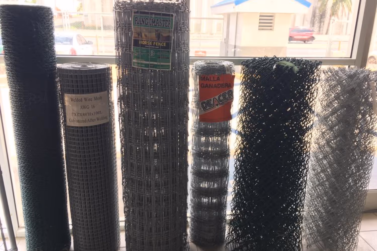 Rolls of welded wire mesh and chain-link fencing displayed in a showroom, representing Ace Construction Supplies’ 2004 innovation in manufacturing cyclone fencing in Puerto Rico.