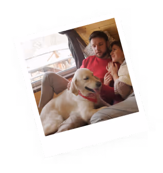 Couple sitting close together on a couch with a golden retriever lying in front of them indoors.