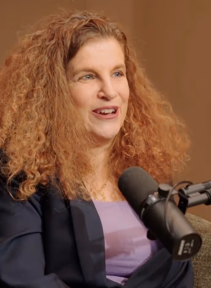 Woman with curly red hair speaking into a microphone during a recorded interview or podcast.