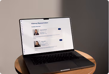Open laptop on a round wooden table displaying a webpage with profile pictures and names under 'Attorney Representation'.