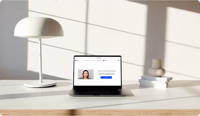 Minimalist desk setup with a laptop displaying a meeting signup page, a white modern lamp, and a small decorative vase on stacked books.
