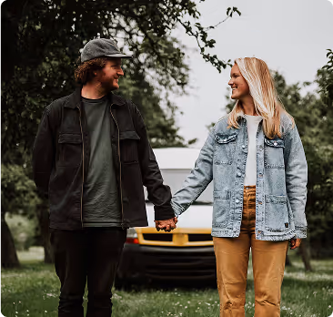 Man and woman holding hands outdoors with a car and trees in the background.