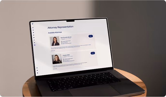 Laptop on round wooden table displaying a webpage titled 'Attorney Representation' with profiles of two female attorneys and 'Book' buttons.