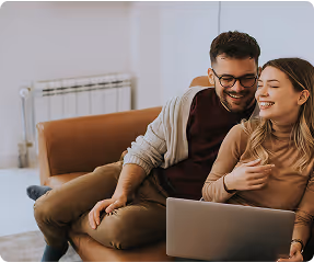 Smiling couple sitting on a couch looking at a laptop together.