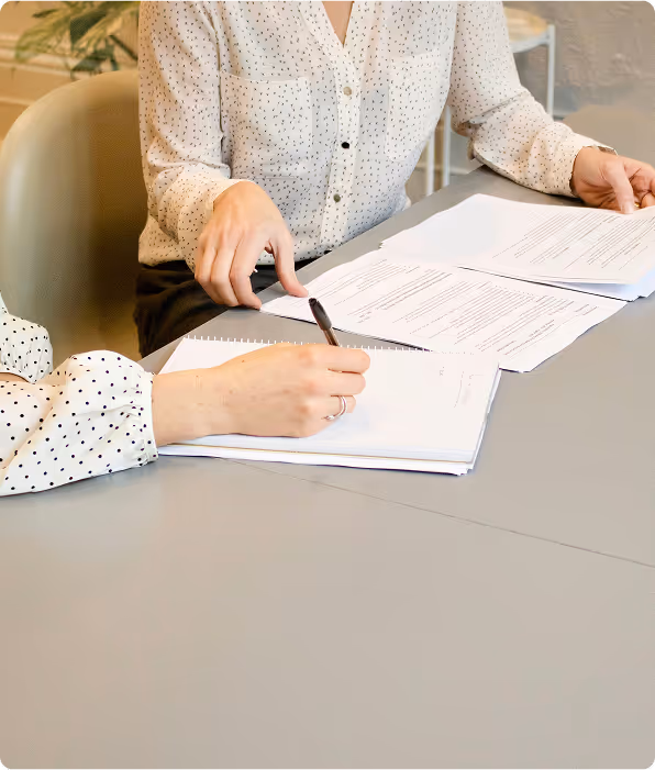Two people at a table reviewing and signing documents with one person writing in a notebook.