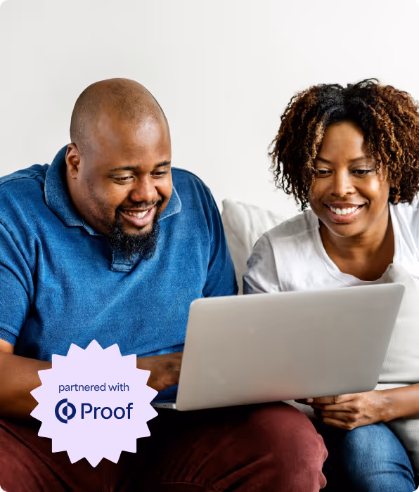 Smiling man and woman sitting on a couch and looking at a laptop screen together.